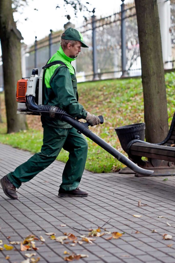 Ein Mann bläst Laub von einem Gehweg weg